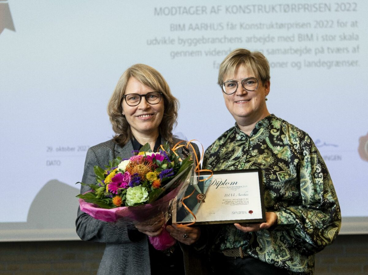 Formand for BIM Aarhus, Marianne Friis (tv.), modtager det synlige bevis på Konstruktørprisen 2022 fra Konstruktørforeningens formand Kirsten Nielsen. Ud over diplomet modtager den filantropisk forening en glasskål designet af Therese Rand og et 'plant et træ'-bevis. Foto: Palle Skov