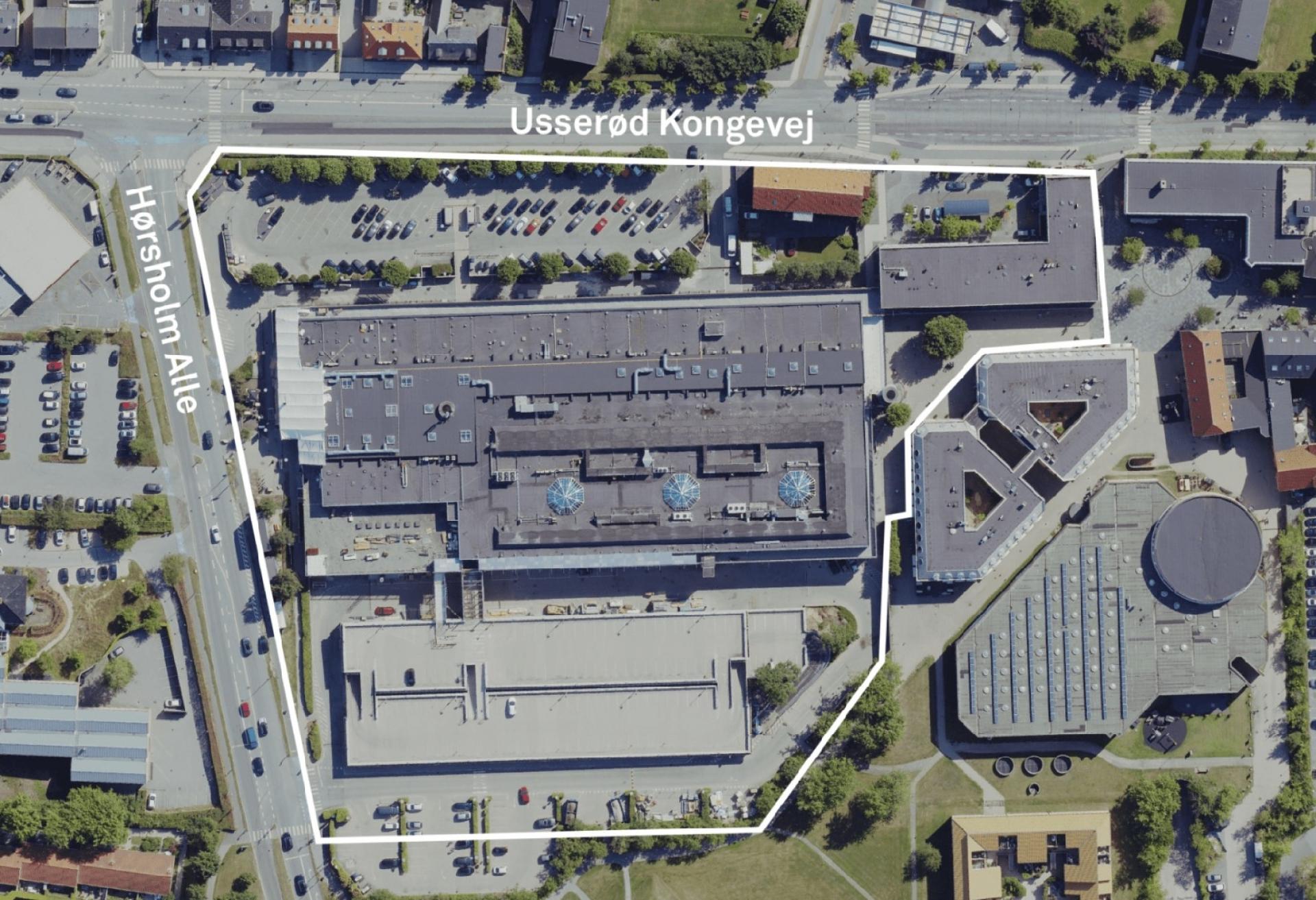 Det knap 30.000 kvm projektområdet set oppefra: Hørsholm Midtpunkt er den store mørkegrå klods, mens det lysegrå nuværende p-hus ses nedenfor. Parkeringsarealet mod Usserød Kongevej bliver omdannet til p-hus, fire byhuse og åbne byrum. Dertil skal der bygges 60 boliger ovenpå det L-formede hus. Den runde cirkel udenfor projektområdet er kulturhuset Trommen. Visualisering: AI Arkitekter & Ingeniører