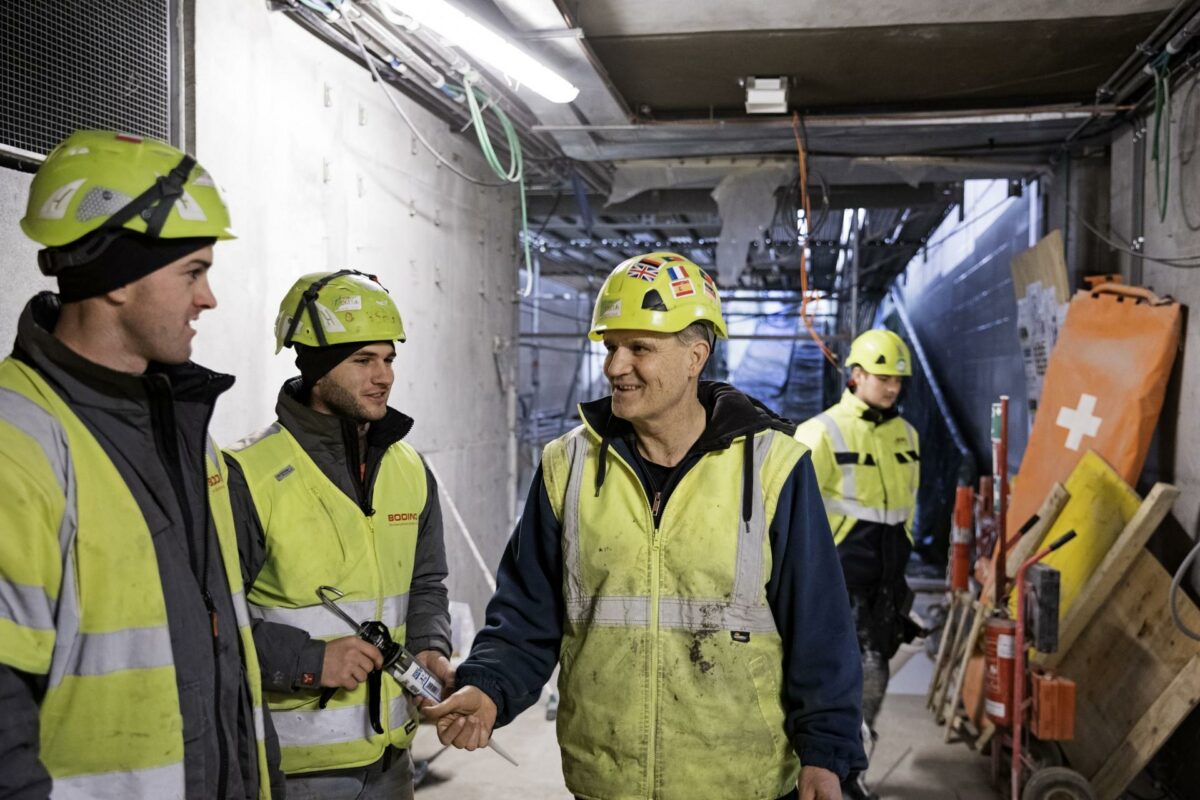 Metrobygger Vitor Gomez fra Canada taler fem sprog, som det ses af flagene på hans hjelm. Det er blandt andet på grund af et øget fokus på samtale, at hovedentreprenøren Copenhagen Metro Team er lykkes med at reducere i ulykkesstatistikken, hævder selskabet. Foto. CMT.