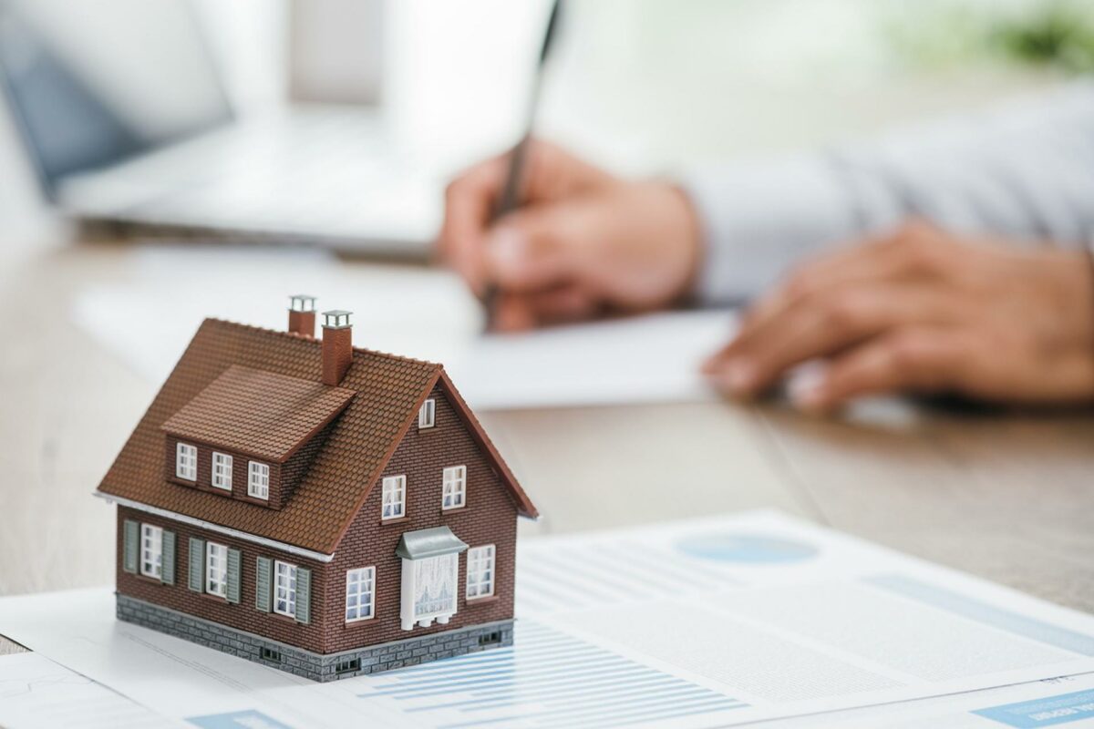 Real estate agent working in his office, he is writing a contract and house model on the foreground: investments, home loan and insurance concept