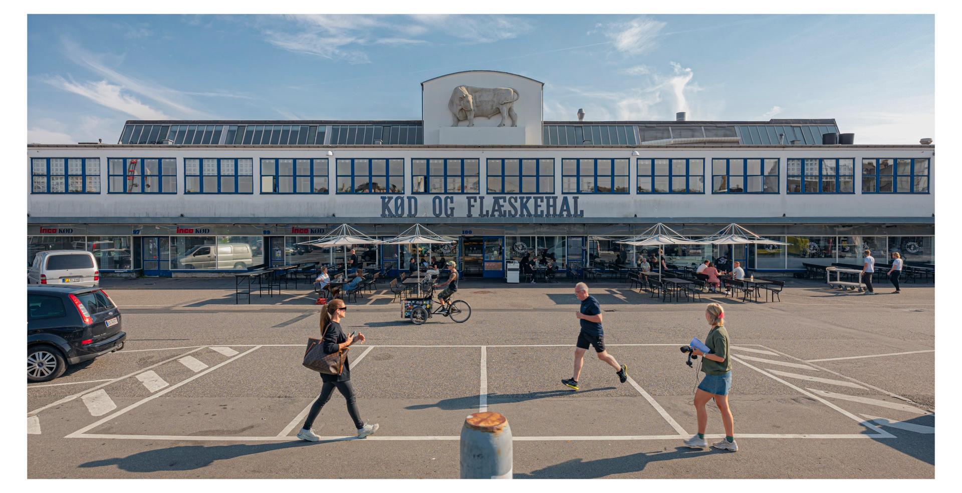 Et eksempel: Flæskehallen Den hvide Kødby I mange år genlød Den Hvide Kødby på Vesterbro af slagternes taktfaste hug, sækkevogne, der skramlede rundt, og råben og snakken fra de mennesker, der myldrede frem og tilbage. Bygningerne var til praktisk brug, med slid og stødmærker på porte og døre. Over det hele lå en lidt fad em af kogt fedt, blod og kød. Der var næppe mange, der dengang tænkte på, at de her færdedes i det, der i dag bliver kaldt epokegørende arkitektur på linje med Arne Jacobsen. Den Hvide Kødby blev opført af Københavns Kommune i årene 1931-34 efter tegninger af stadsarkitekt Poul Holsøe og hans medarbejdere. Og det med lige linjer, glatte overflader og en hvidhed, der signalerede hygiejne. I dag er hele området sat i stand og en magnet for et yngre, tjekket publikum, som skal hen og have noget at spise og drikke eller lige skal købe den helt rigtige kniv til den hjemmelavede Sushi. De udstillede tegninger giver et enestående overblik over Kødby-komplekset, mens s/h fotos giver et nostalgisk tilbageblik og Jens Marius Lindhes fotos viser, hvordan det tager sig ud i dag. Foto: Jens Markus Lindhe.