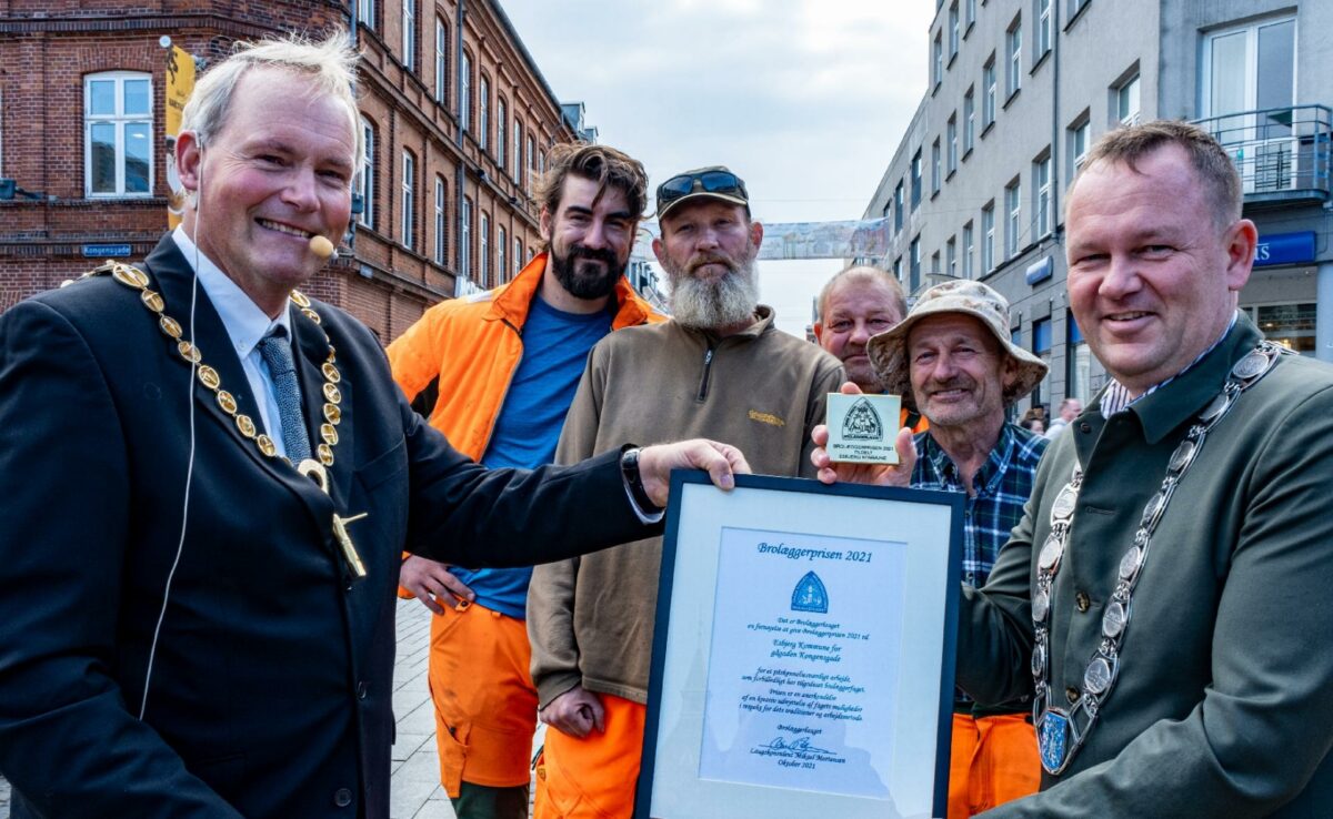 Oldermand i Brolæggerlauget Claus Johnsen overrækker Brolæggerprisen til borgmester Jesper Frost Rasmussen på torvet i Esbjerg, mens brolæggere fra Arkil-Stürup ser til. Foto: Klaus Hybler.