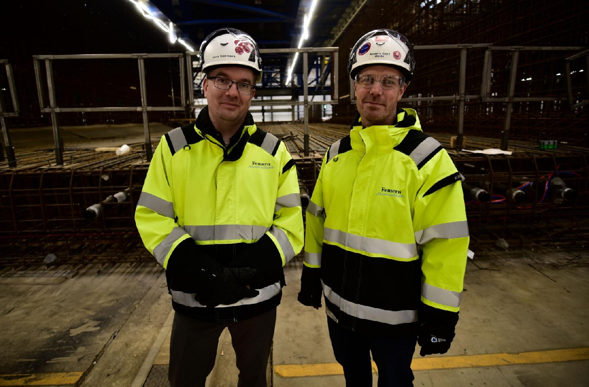 Pressechef Jens Villemoes og Construction Area Manager Anders Gert Wede ses her foran en af de færdige armeringskonstruktioner, som skubbes ind i støbehallen. Betonblandeværkerne har en kapacitet på 600 kbm beton i timen, en kapacitet, der dog kan øges til 700 kbm i timen, hvis der er spidsbelastning, men realistisk set anvendes 200-300 kbm beton i timen. Hvert element vejer 73.500 tons. Foto: Henrik Malmgreen