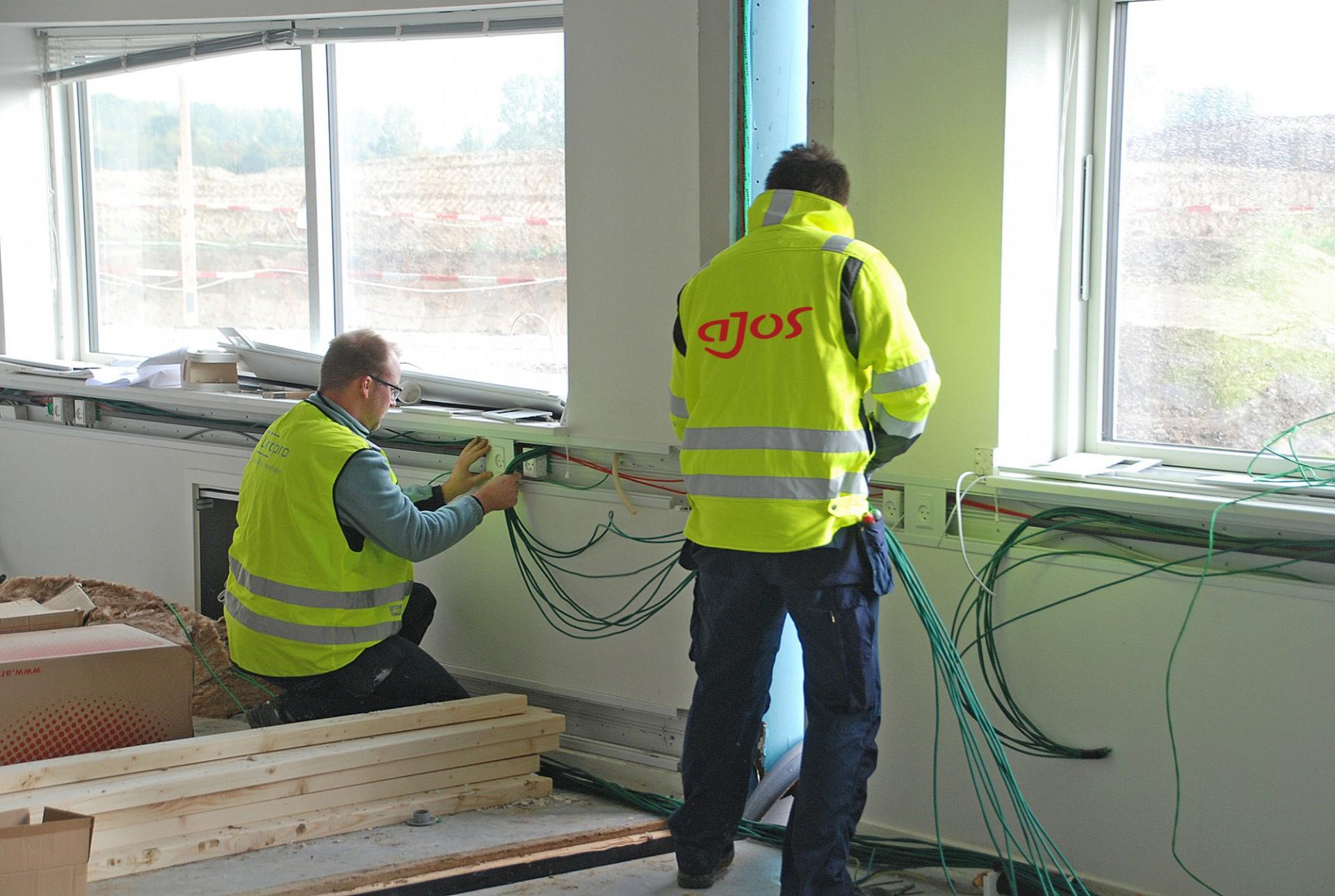 Elektrikere i gang med at forbinde installationerne i pavillonerne til besøgscenteret ved byggeriet af det nye universitetshospital i Odense.