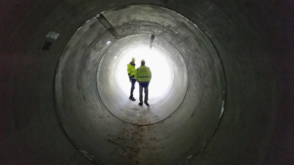 To mænd i gule refleksjakker står inde i en stor tunnel. Der er højt til loftet.