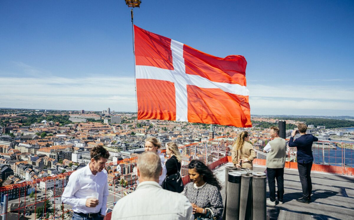 Gæster til rejsegilde er samlet på toppen af det 114 meter høje Akson. Et stort dannebrogsflag hænger fra en kran. Udsigten over Aarhus er fin.