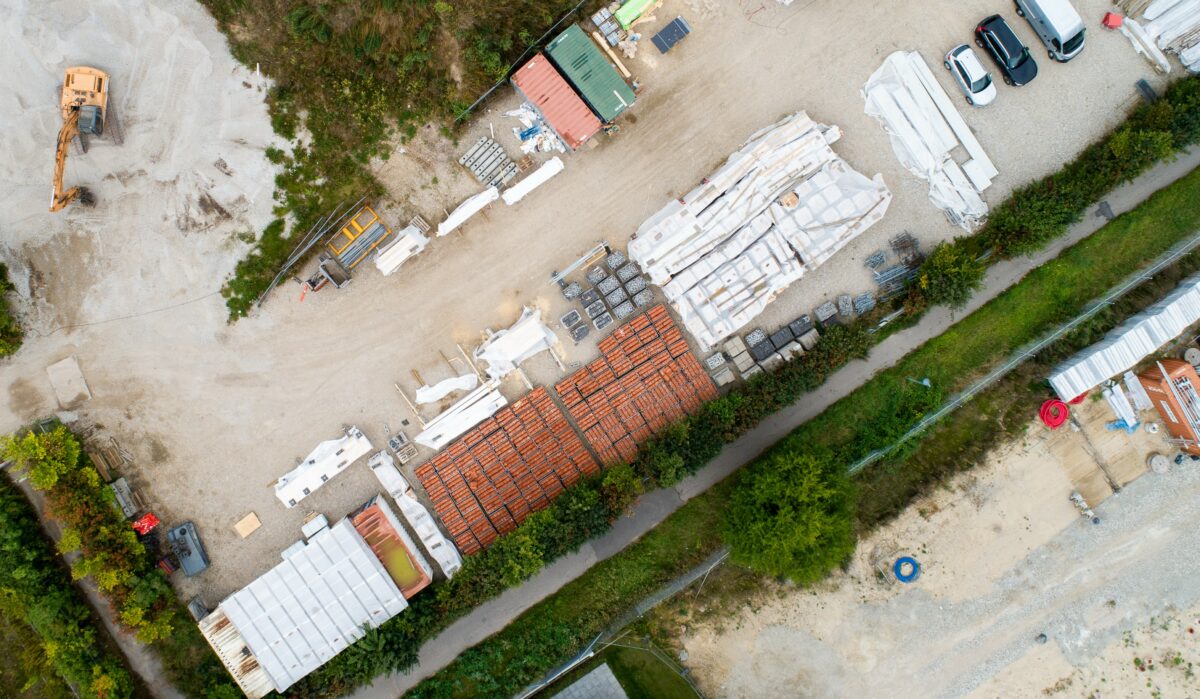 dronefoto af byggeplads med byggematerialer på række, tegl, træ og maskiner
