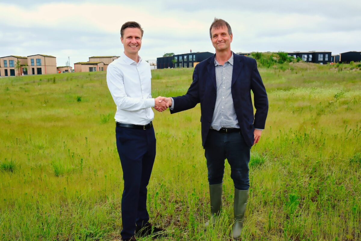 Christopher Tranæs og Morten Pedersen giver hånd på et græsareal med boliger i baggrunden.