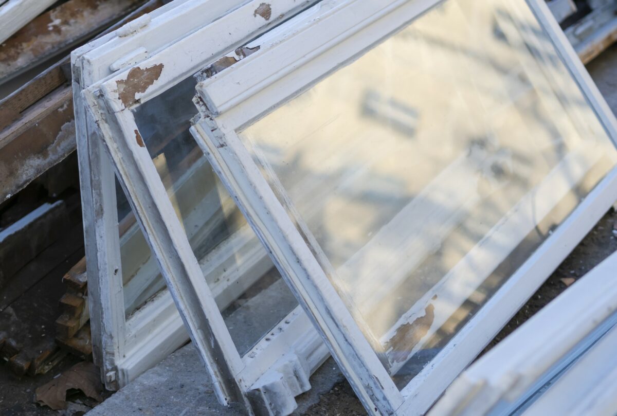 Gamle vinduer, hvor den hvide maling er skallet af, står lænet op ad hinanden.