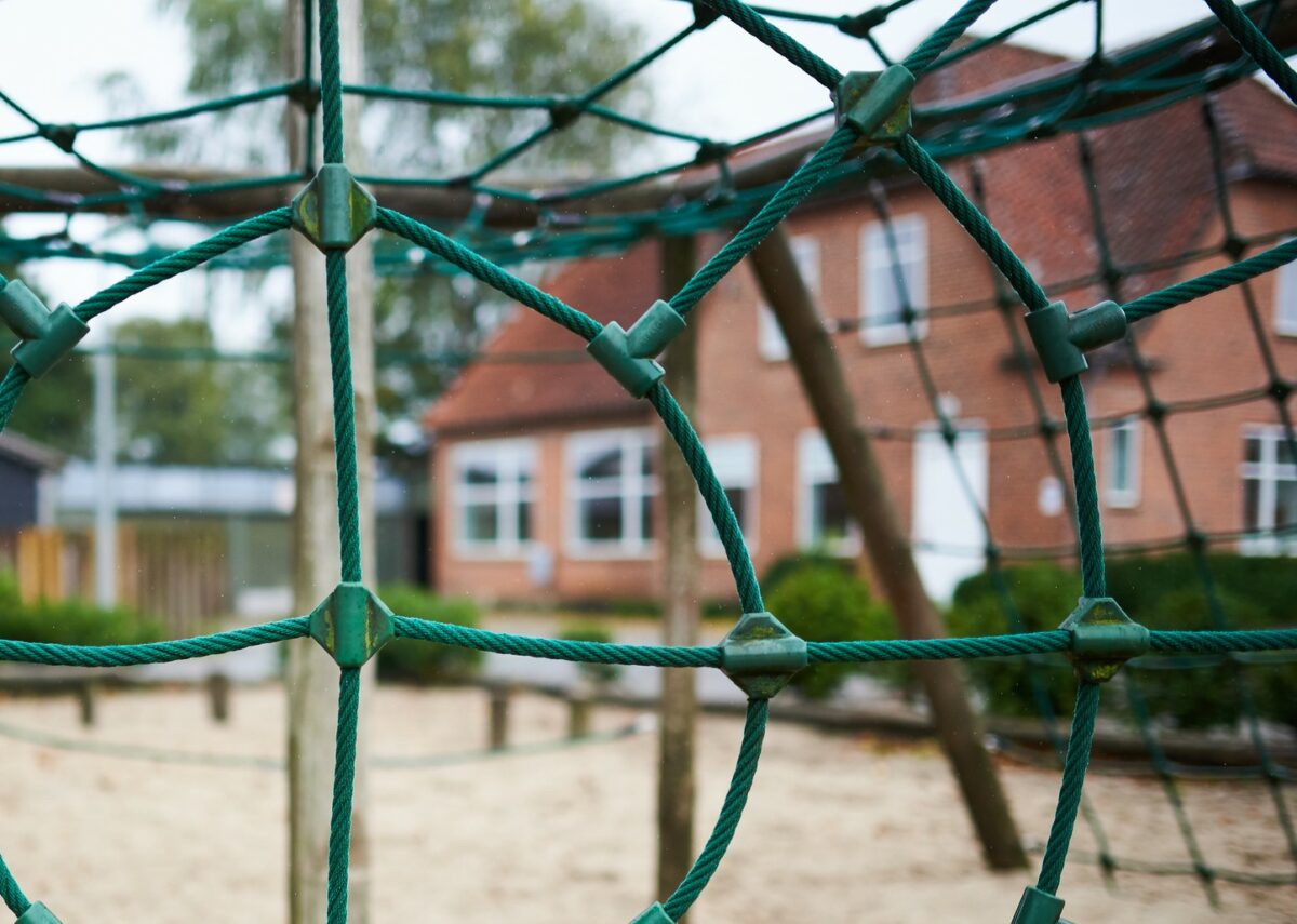 En rød skole set gennem et grønt klatrenet, der er holdt sammen af grønne plasticknopper