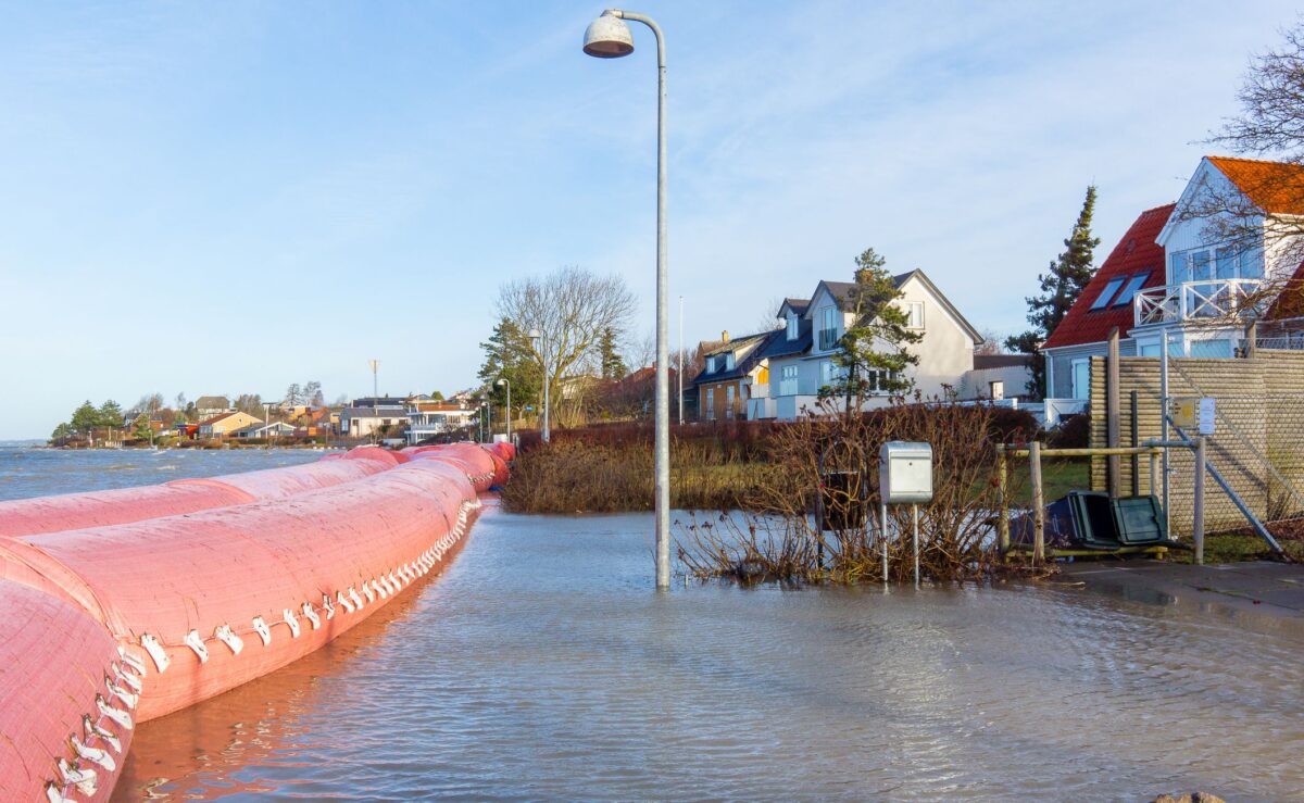 en orange watertube ligger i vand foran en række huse til højre. En grøn skraldespand er væltet og ligger åben i vandet