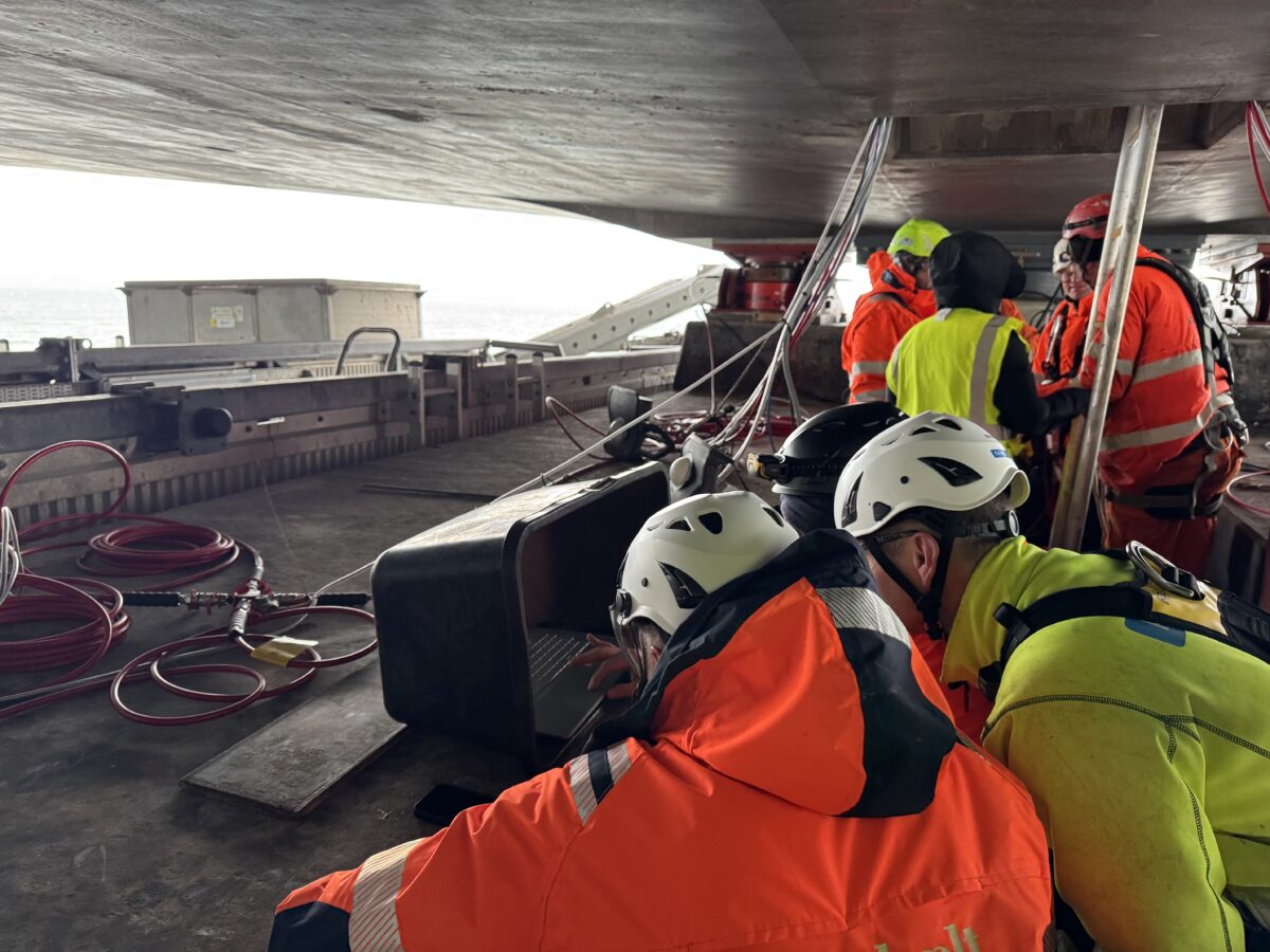 Foto av en gruppe mennesker i oransje og gult sikkerhetsutstyr som sitter konsentrert under broen