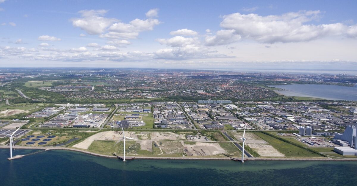 Luftfoto af Avedøre Holme med vindmøller langs kysten, industri og længere inde på land boliger