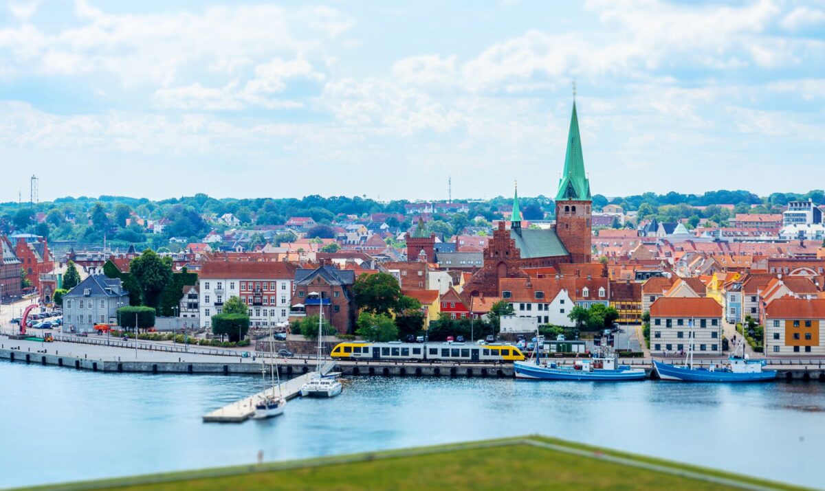 Foto af Helsingør by set fra Kronborg. Der kører et gult og gråt tog fra lokalbanen foran bygningerne. Bag toget knejser det grønne kirketårn