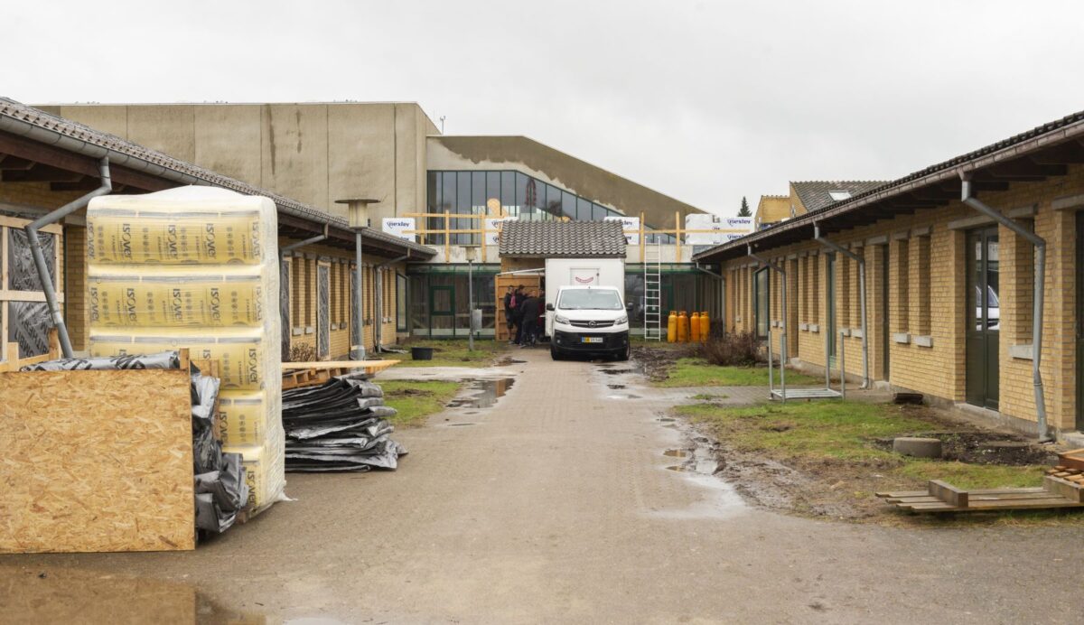 Foto af en gammel skole. Udenfor er der byggematerialer bl.a. baller af isolering. En varevogn er bakket ind foran skolen for enden af en bred sti