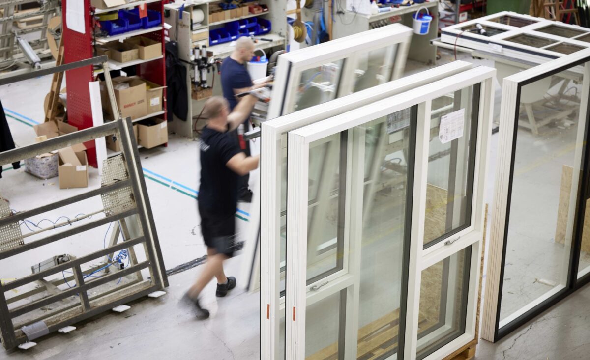 foto fra en vinduesfabrik. En mand i sort t-shirt går mellem en stor samling opretstående vinduer