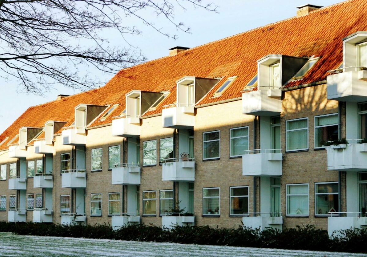 Foto af boligejendom i gule mursten med rødt tag og hvide altaner