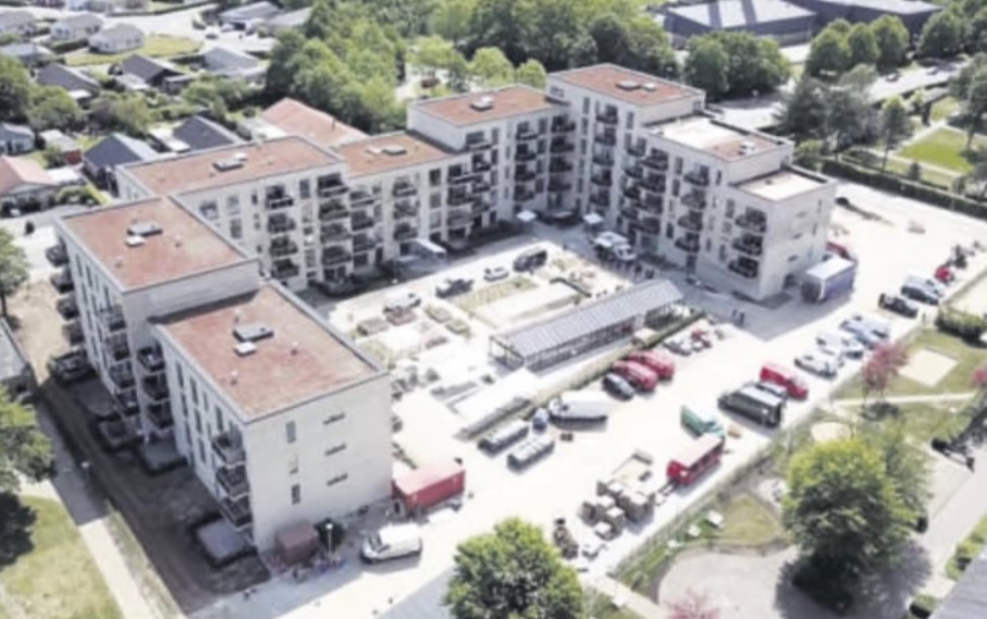 luftfoto af et trlænget boligbyggeri med et langt orangeri i gårdrummet