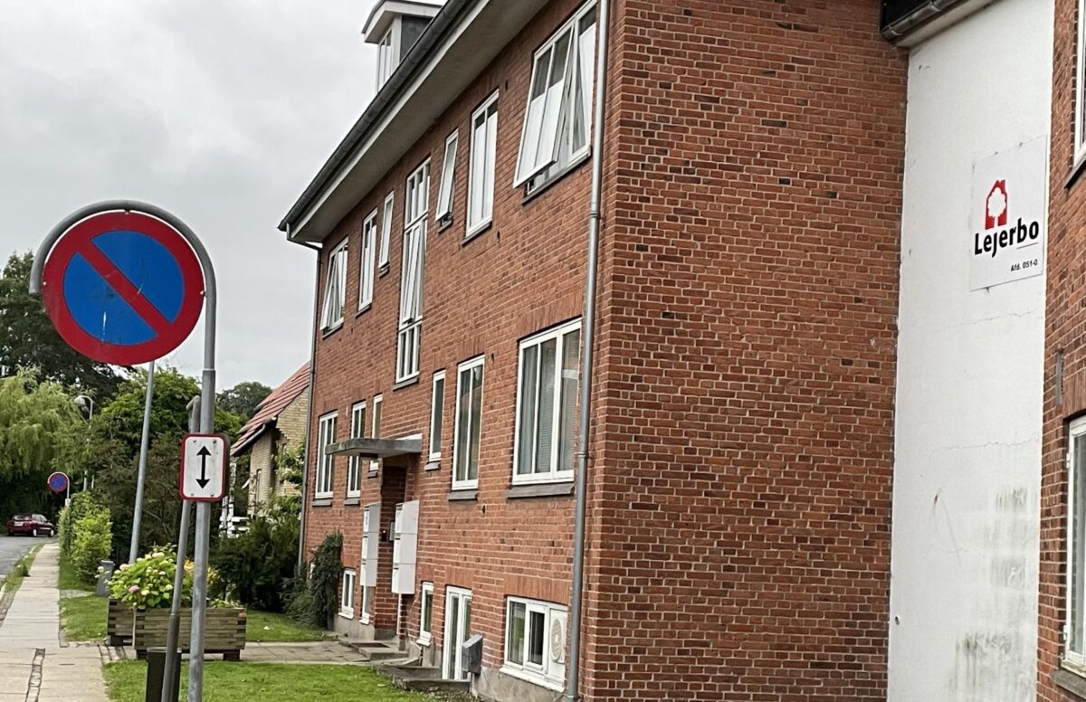 Et rødt muret hus i to etager set fra siden langs vejen. Der står Lejerbo på en hvid væg, der forbinder bygningen med en anden