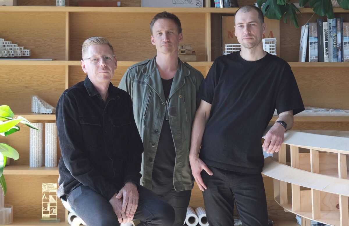 Tre mand på stibe foran en reol med planter og bøger