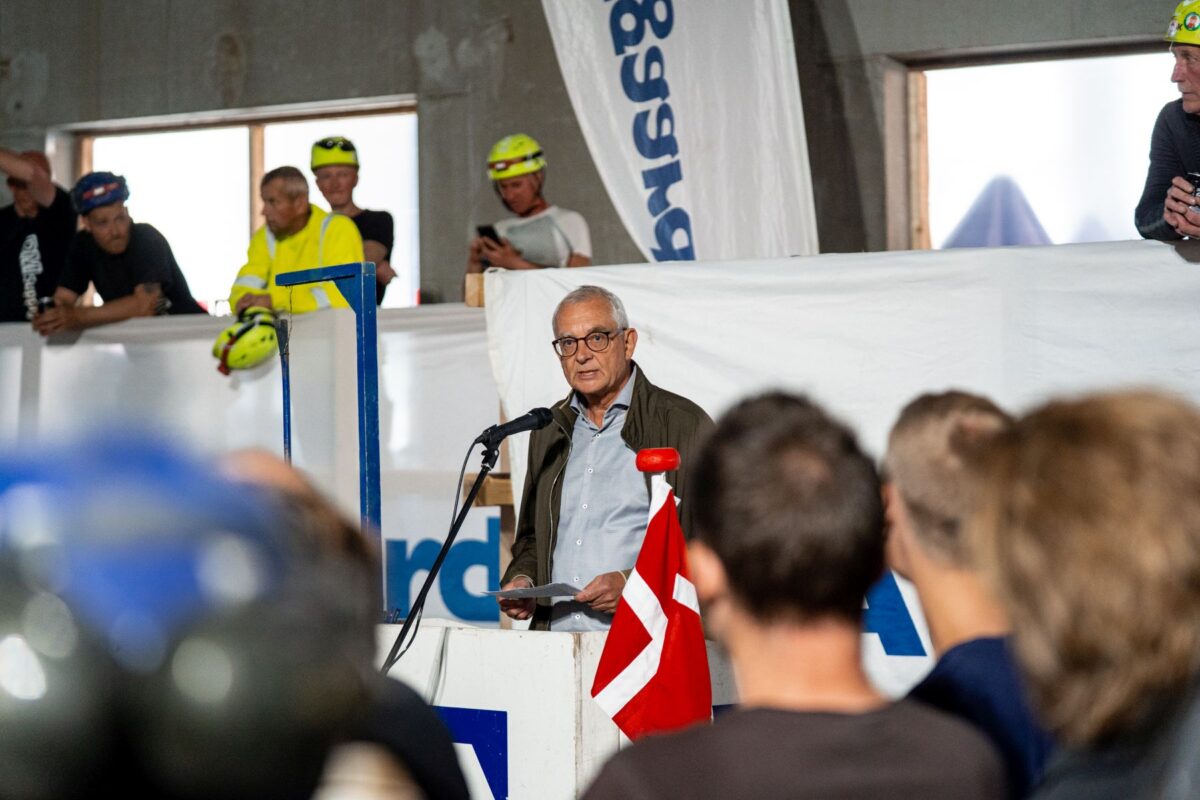 En mand på en talerstol taler til de mange mennesker, der står omkring ham. Et dannebrogsflag står foran ham