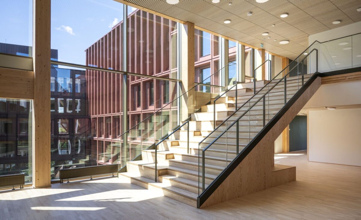 Foto indefra WoodHub hvor en trappe i træ fører opad. Udenfor vinduet ses sidebygningen