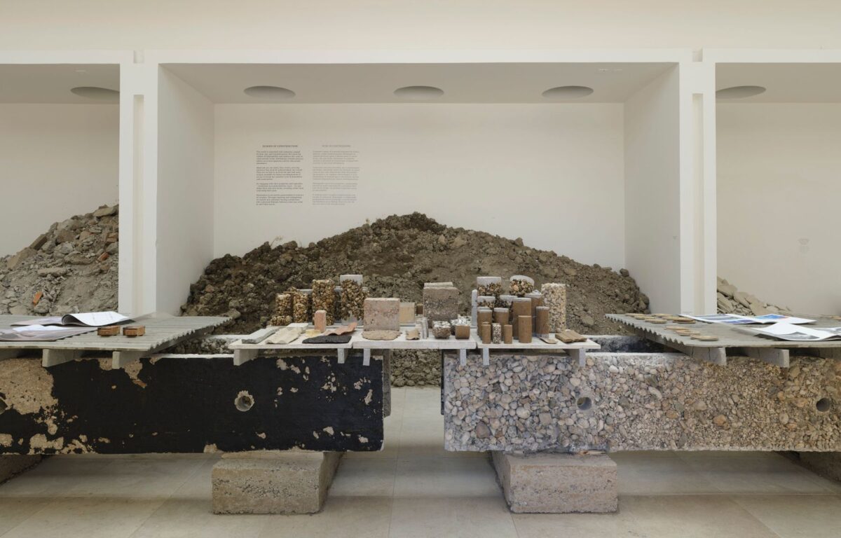 Foto fra en indendørs byggeplads medstore slabs fra gulvene lagt op som borde. I baggrunden bunker af grus og sand mv.