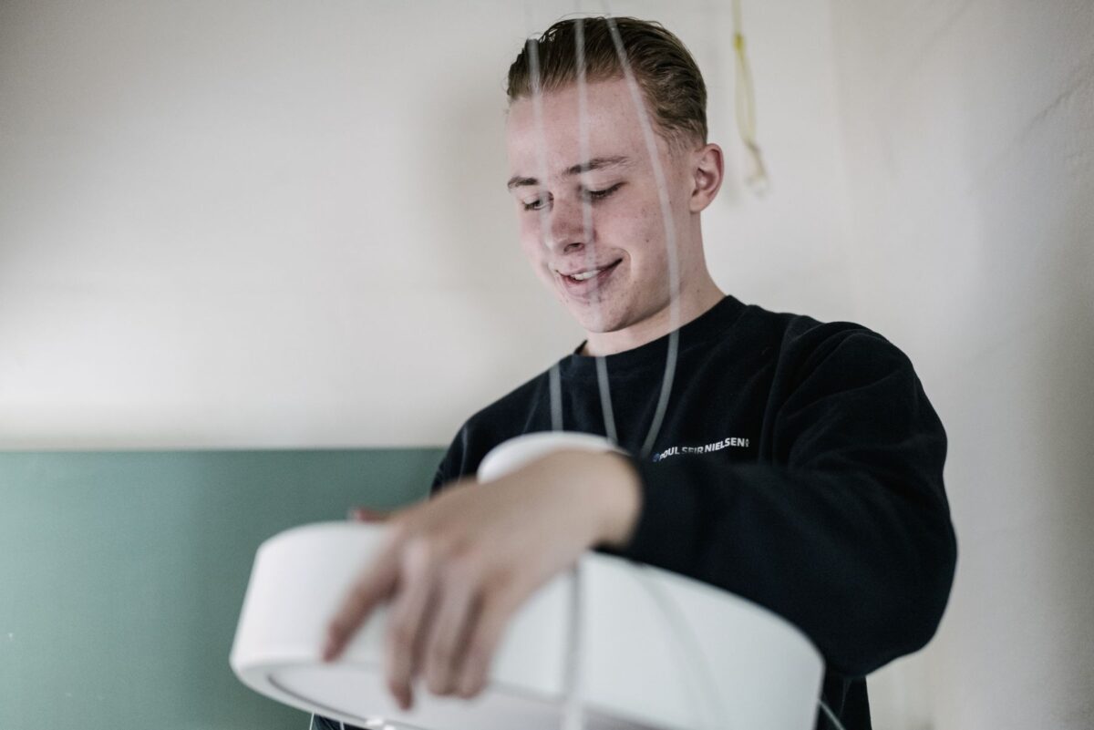 Ung elektriker i mørkeblå sweatshirt holder en rund hvid lampe i armene