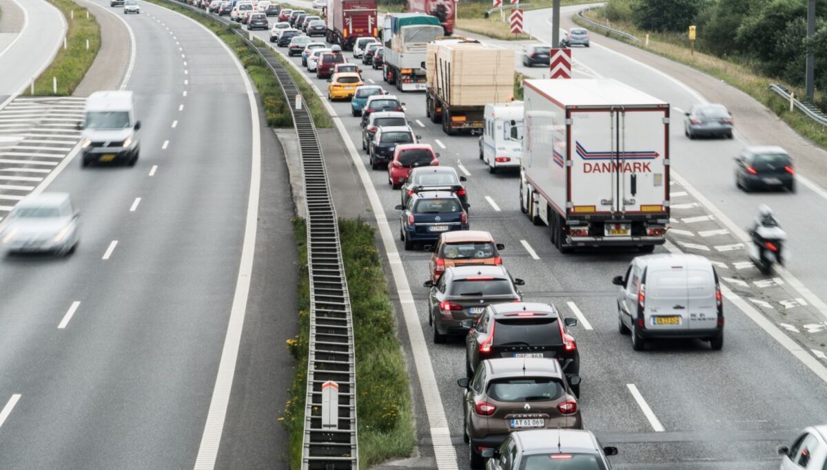 Foto af en motorvej, hvor der er kø i den ene side. I den modkørende retning kører bilerne hurtigt og med afstand