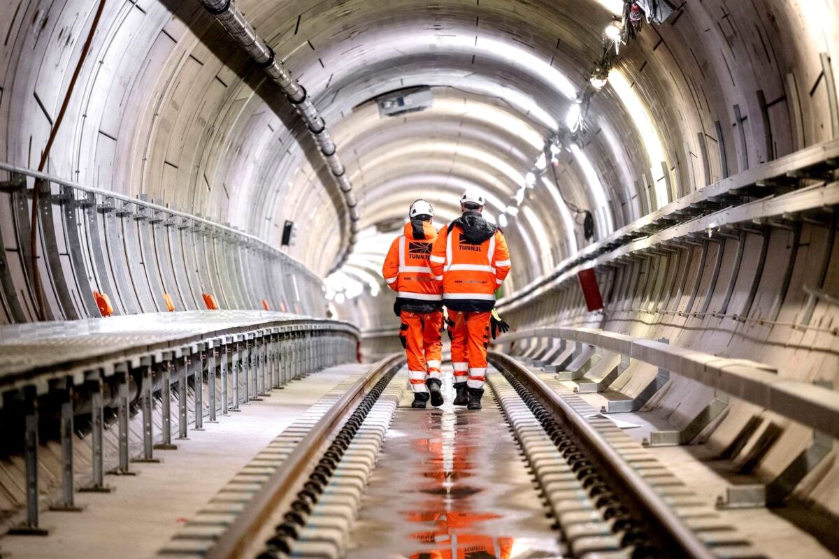 To mennesker i orange arbejdstøj går gennem en metrotunnel.