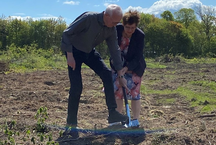 Foto af en mand og en kvinde der hjælpes lidt akavet ad med at tage første spadestik