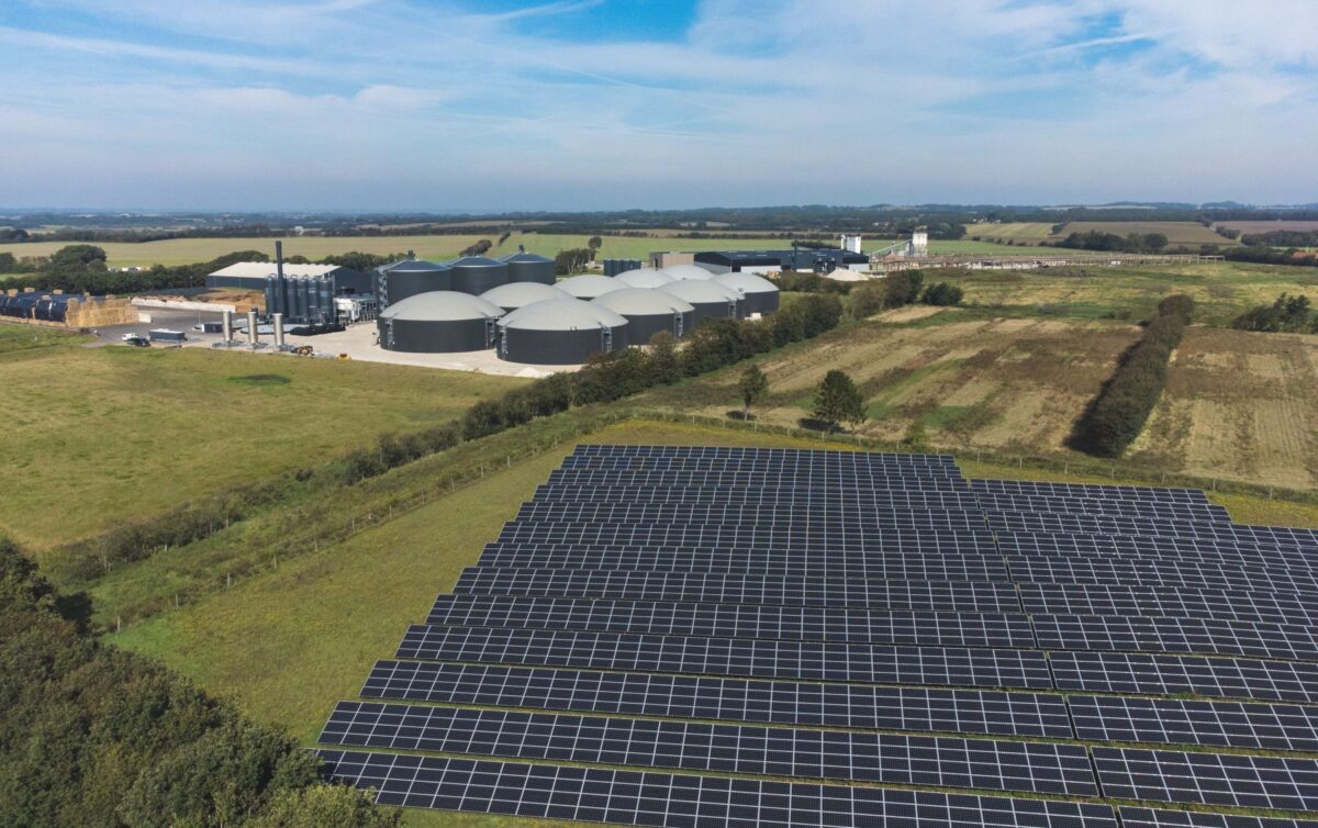 Solcelleanlæg ses i forgrunden af et biogasanlæg med store hvide cylindre